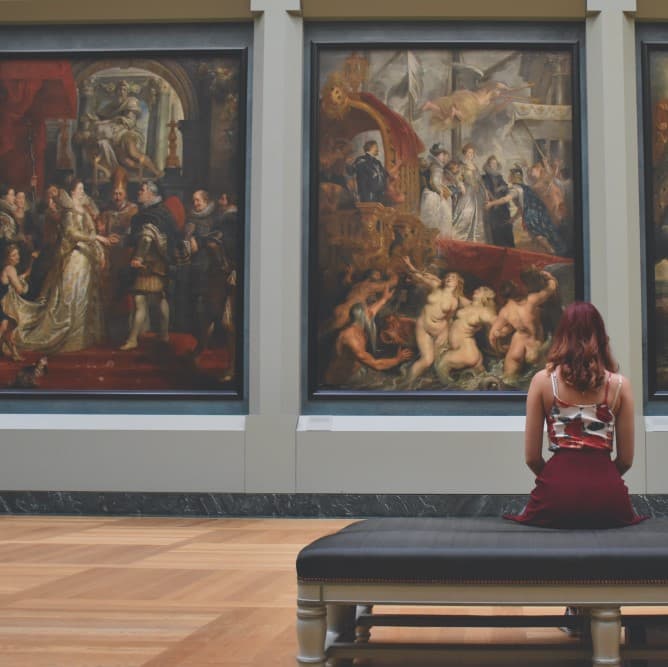 Foto de una chica sentada observando cuadros en un museo.